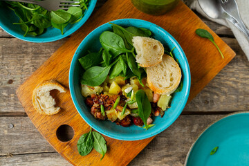 Potato, bacon and sausage salad with fresh spinach served on cutting board, top view