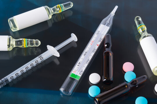 against the background of a photograph of a person with suspected coronavirus, a syringe with a preparation, tablets, ampoules, a thermometer for measuring body temperature, close-up