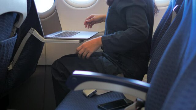 Safety travel. Young woman fasten belts while sitting in airplane seat and working on laptop.