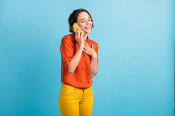 Photo of pretty funny lady good mood hold telephone communicating listen best friends joke funky story laughing out loud wear orange shirt yellow trousers isolated blue color background