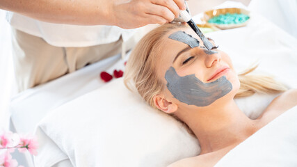 Skin face care and Beauty treatment concept.Beautiful young attractive Caucasian woman masking face with natural clay for skin care and having massage by Thai Masseuse in aroma spa salon.