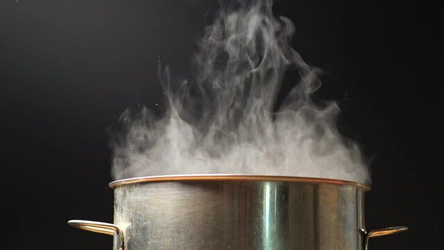 Steam comes out of the pan during cooking. Boiling water in pan on a black background. Slow motion shot