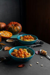 Millet porridge with pumpkin and honey served in blue bowls, raw pumpkins and seeds. Image has copy space