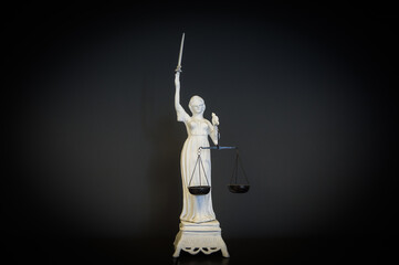 White figurine on black background of the goddess of a Themis with scales in a hand and a bandage...