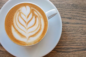 Cappuccino coffee dressing with leave shape of latte art on wood table,