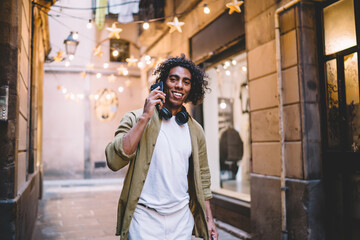 Fototapeta premium Smiling young black guy talking on smartphone on street