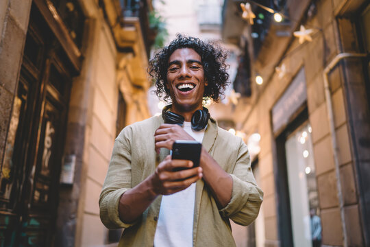 Happy man using smartphone and headphones on narrow street