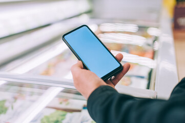 Mock-up technology. The guy holds a smartphone in his hands on the background of showcases in a supermarket.
