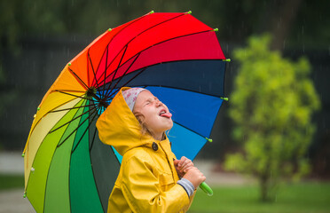 happy kid catching rain drops in park. Funny little girl playing under the autumn rain. Kid wearing...