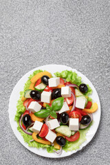 Greek salad with cheese and fresh vegetables on grey background.