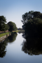 pleasure boats on the canal, calm day with clear reflection on the water, trees and blue sky