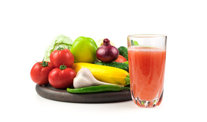 A glass of fresh vegetable juice and a Large selection of fresh vegetables on a round tray on a white background. Plant background. The concept of proper nutrition.
