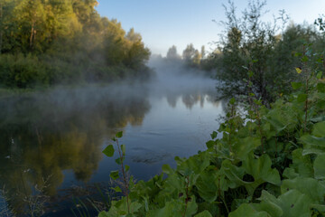 Autumn time. Dawn over the river in a misty, brooding haze. Beautiful view of the forest and river, covered with fog in the early morning. The sun's rays of light.