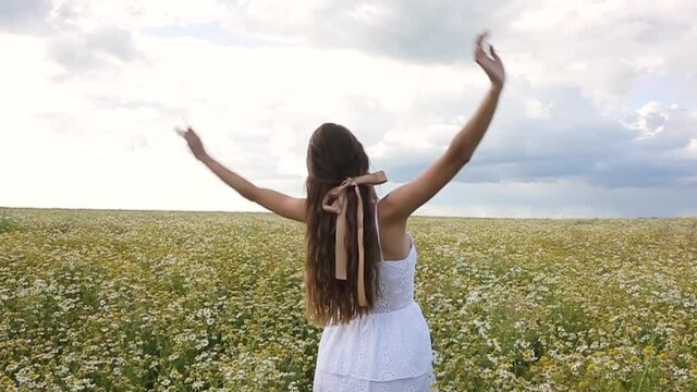 young woman long hair and white dress in the field chamomile on the summer Blue skyline