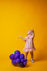 small child poses on a yellow background with balloons in the form of grapes