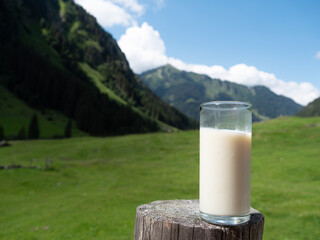 A glass with a fresh milk on a  wooden fence with mountains in background.