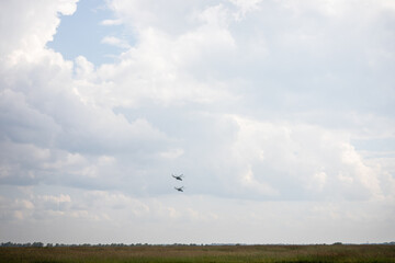 two helicopters fly against the sky with clouds