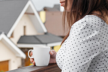 Young woman standing with a white cup in her hands and watching on the modern houses. Building of house of dream. Advertising concept for architecture company. Good neighborhood