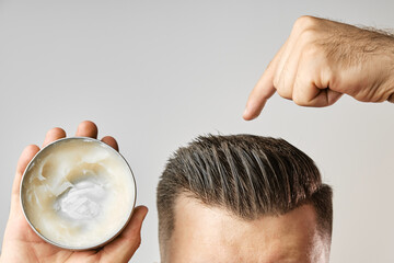 Man applying a clay, pomade, wax, gel or mousse from round metal box for styling his hair after barbershop hair cut. Advertising concept of mans products. Treatment and care against lost of hair