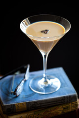 Creamy, tan espresso martini with floating coffee beans, single glass