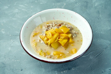 Appetizing and healthy oatmeal with mango and chia in a white bowl on a gray background