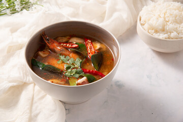 River prawn spicy soup in white bowl and rice in right corner decorate by white fabric on white table for restaurant and street food commercial stock photo