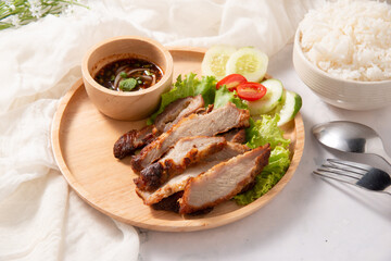 kho mhoo yang, fired slice pork decorate by salad tomato and cucumber serve with spicy sauce in wooden round plate lay on white table with rice fork spoon for menu design stock photo