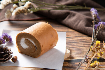 slice coffee roll cake on white rectangle paper and wooden plate decorate by dry flower on wood texture table in morning mood stock photo