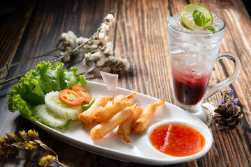 shrimp warp or ebi roll deep dry in white ellipse dish fill with spicy source decorate by slice tomato cucumber beside red soda topping mint leaf in dry flower on wood table texture, trepezoid flag
