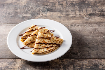 Sweet crepes with chocolate on wooden table.	Copy space