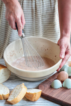 Woman's hands preparing French toast batter with farm fresh organic eggs and a loaf of bread nearby.