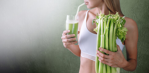 Portrait of a young woman with a bunch of celery in one hand and a glass of celery juice in the...