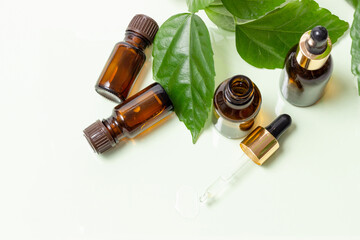 Glass cosmetic bottles with a dropper stand next to green leaves on a white background. Organic cosmetics concept, natural essential oil and cream