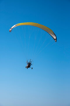A paraglider with a yellow parachute against a clear blue sky.