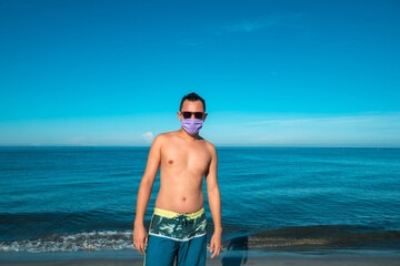 Hispanic man with sunglasses and a mask for the pandemic on the beach