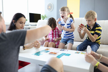 Adults and children are sitting at table and holding playing cards girl stood up and shouts. Child cannot play concept