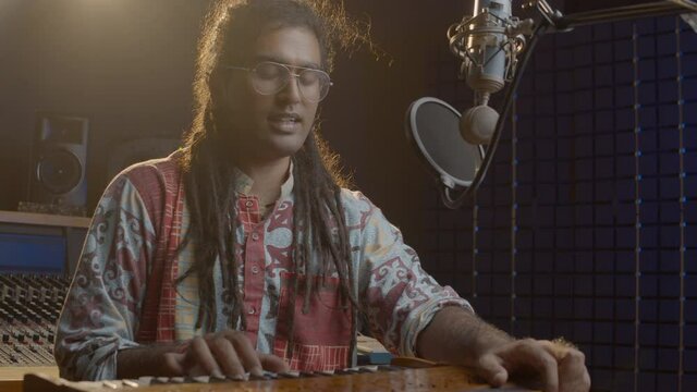 Music production studio. Creative world. Hindi man playing harmonium in the sound studio. A long hair brunette male person in a traditional shirt plays meditation music.