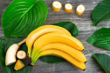 Bunch of raw organic yellow bananas with slices and green leaves on wooden background - 376961325