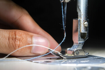 Fingers hand of seamstress with needle presser foot and blue thread of industrial sewing machine to for sew cloth close-up.
