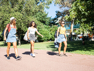 Three young mixed race female friends walking together in the park smiling with sunglasses - Two Caucasian women take a fun walk in the nature in the city with a Hispanic woman in casual wear