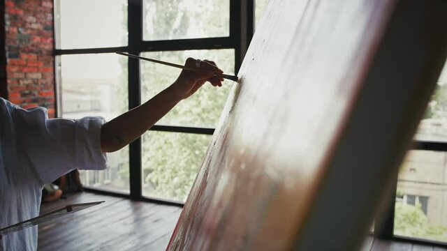 Hand of unknown woman artist who drawing a portrait on canvas in modern art style against huge window of studio