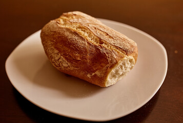 Pan ciabatta servido en una mesa de madera.  Pan recien horneado. Pan sobre plato de porcelana blanca
