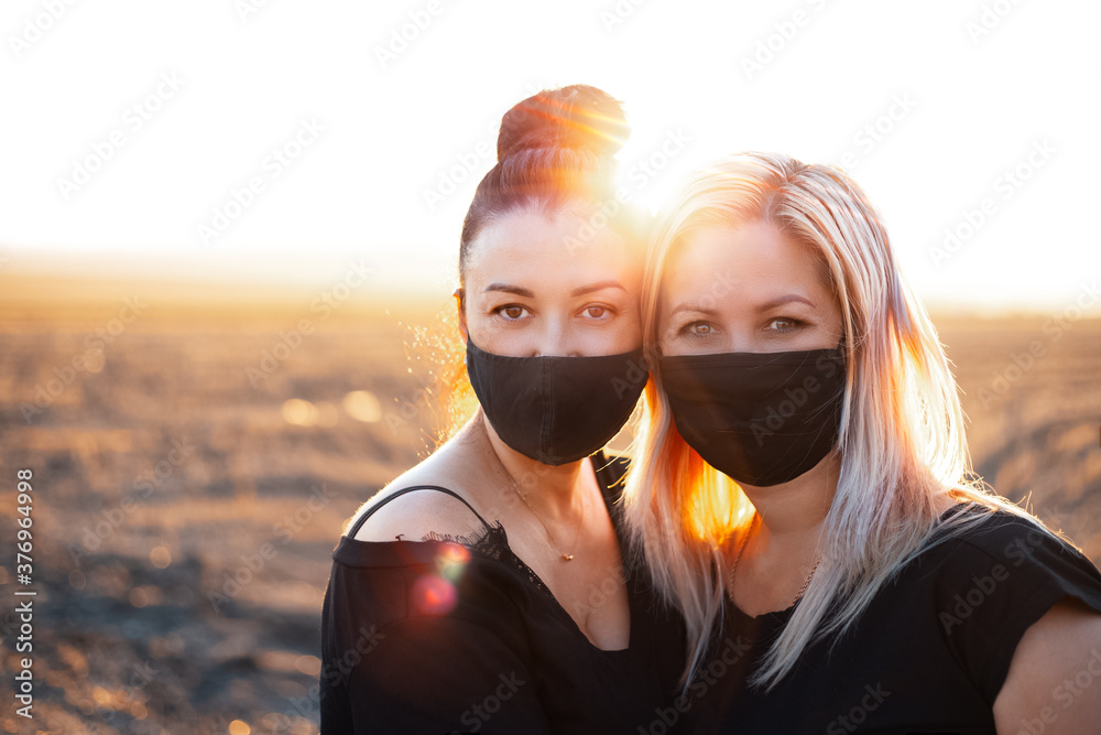 Wall mural Outdoors portrait of two women, wearing respiratory face mask on the background of sunset.