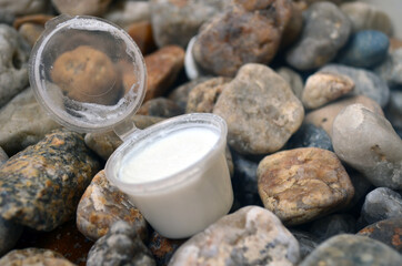 An open jar of white cream for body and face care against a background of sea stones.