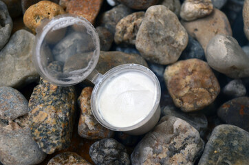 An open jar of white cream for body and face care against a background of sea stones.
