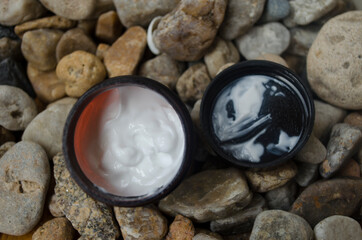 Fototapeta na wymiar An open jar of white cream for body and face care against a background of sea stones.