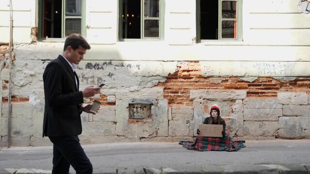 Businessman with coffee and phone walks past a homeless girl.