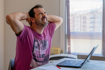Worried bearded man dressed in a purple t-shirt looking at the laptop