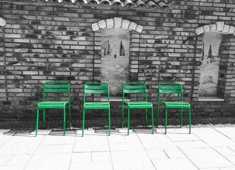 Zielone metalowe krzesła na tle czarno-białego ceglastego muru. Śródziemnomorska sceneria. - obrazy, fototapety, plakaty