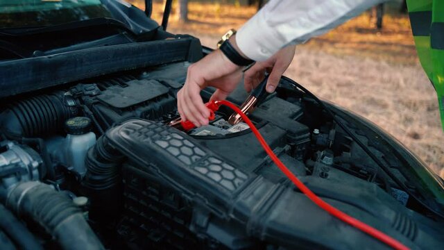 man Charging car battery with electricity trough jumper cables. Charging car battery with electricity trough jumper cables. close up of a  man using jumper cables to start a car battery.